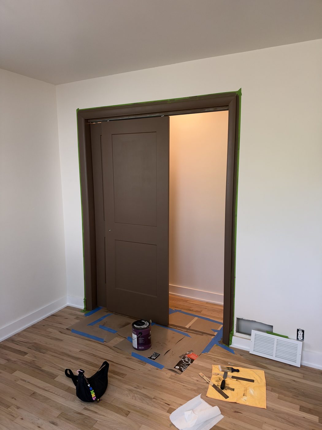 Sep 27, 2026. A brown door mid-paint, taped off beside the hardwood floor
