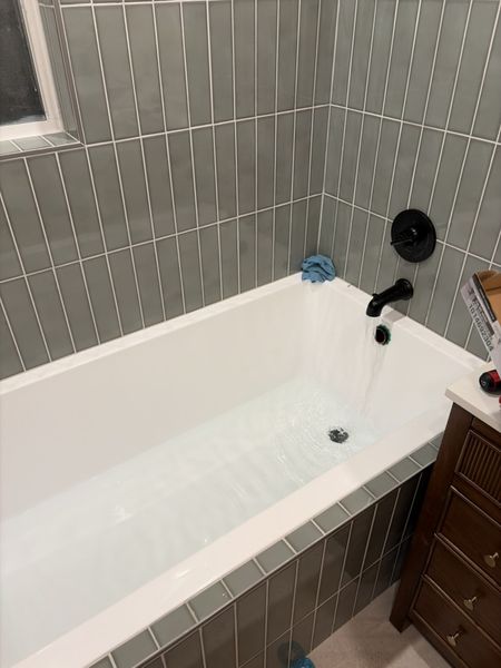 Sep 5, 2026 — Water running into the white tub beneath sage green tile and a black faucet