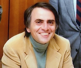 Carl Sagan smiling in a tan jacket and turtleneck in 1980.