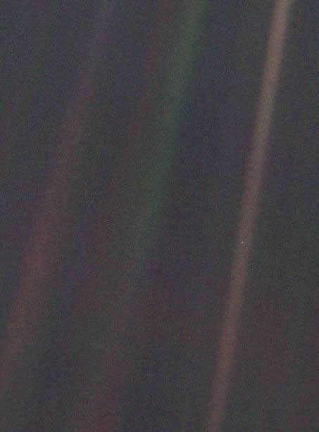 Voyager 1's Pale Blue Dot: Earth is a tiny bright speck near the right side, inside a diagonal sunbeam against dark space.